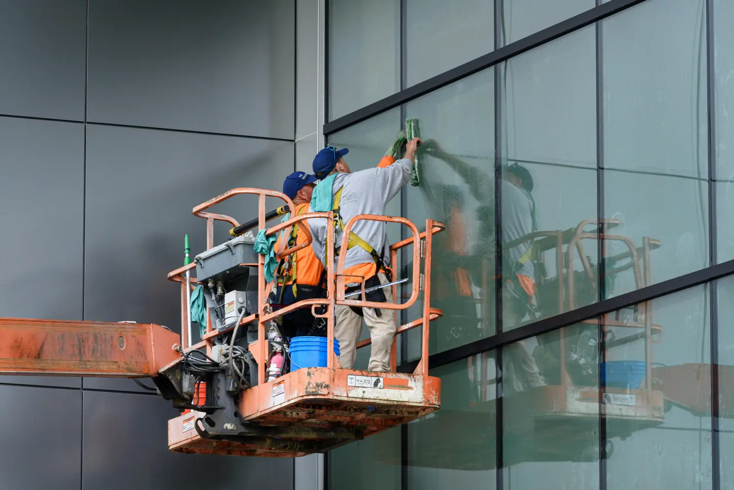 Fensterputzer arbeiten mit einer Hebebühne an einem modernen Glasgebäude. Von AAK-Dienstleistungen